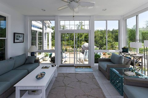 A Florida Room Pictured from Inside with Gray-Blue and White Furniture, White Tile, and White Framing and a Big Yard Outside  